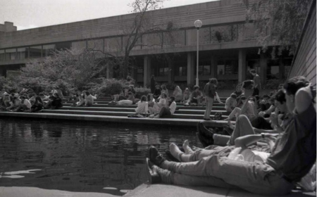 Black and white photograph of students lounging by the main lake on a sunny day. UCD James Joyce Library in the background.